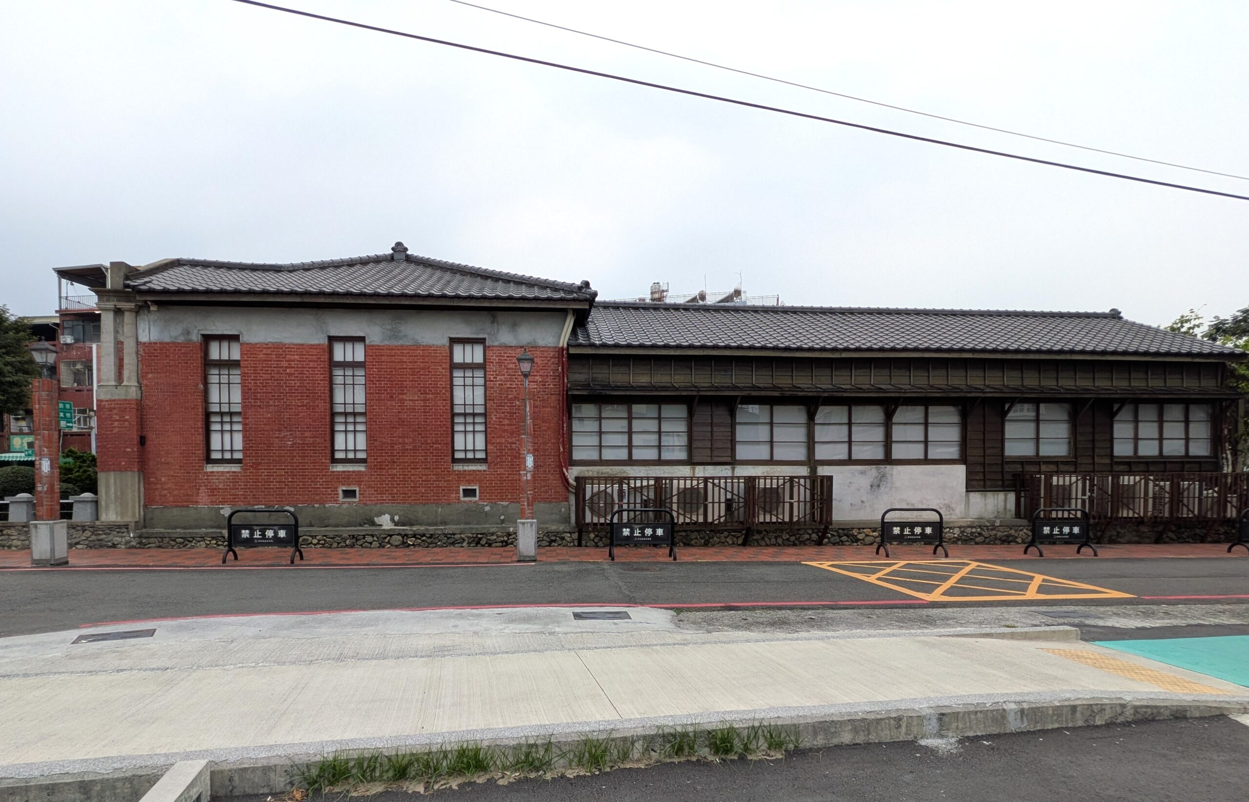 赤レンガ造の建物と奥に延びる木造の長い建物が接続する屏東戯曲故事館の側面外観。