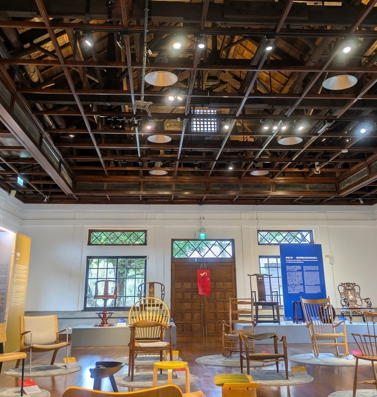 木製椅子の展示と上部に見える木造小屋組の構造。