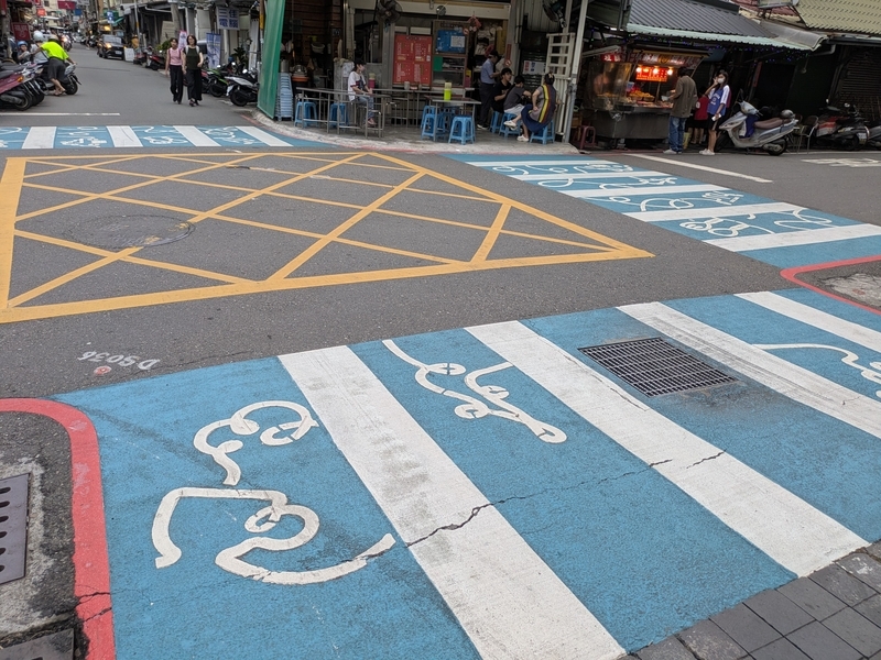横断歩道にシンボルカラーの水色と糸（線）アートが描かれている様子を撮影した写真。